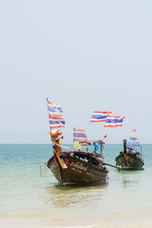 Krabi, Thailand - March 2019: long tail wooden boats with Thai flags moored at Railay beach. Vertical orientation.のeditorial素材