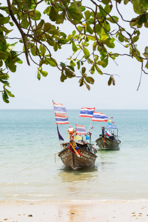 Krabi, Thailand - March 2019: long tail wooden boats with Thai flags moored at Railay beach. Vertical orientation.のeditorial素材