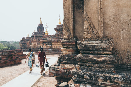 Bagan, Myanmar - March 2019: Two women in traditional dresses walking next to the Buddhist temple of Bagan, Myanmar.のeditorial素材