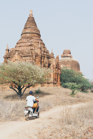 Man riding electric scooter towards temples and pagodas of ancient Bagan in Myanmar. Vertical...