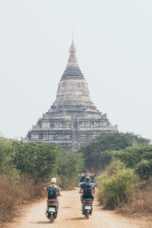 Young couple riding electric scooters towards Shwesandaw pagoda of ancient Bagan temple complex in Myanmarの写真素材