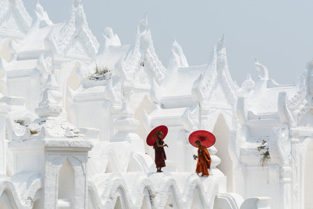 Mandalay, Myanmar - April 2019: Buddhist novice monks in orange robes with red umbrellas walking on the walls of Myatheindan Pagoda.のeditorial素材