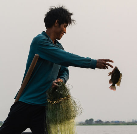 Inle, Myanmar - March 2019: Traditional Burmese leg rowing fisherman at Inle lake catching fish with his handのeditorial素材