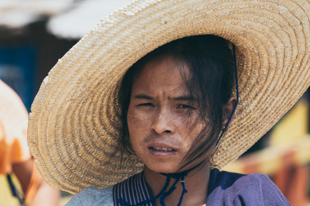 Indein, Myanmar - March 2019: portrait of a young Burmese woman in a big straw hat and tanaka on her...
