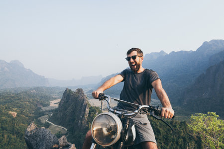 Caucasian young man riding vintage motorcycle on top of the mountains in Vang Vieng, Laos.の写真素材