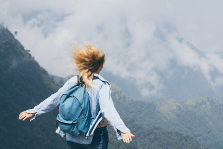 Caucasian blonde young woman drinking coffee on Tram Ton pass overlooking mountains around Sapa in Vietnam. Hands up, wind in hair.の写真素材