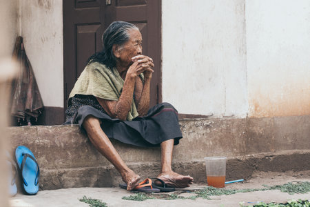 Luang Prabang, Laos - May 2019: old Lao woman sits on the house porch, thoughtful look.のeditorial素材