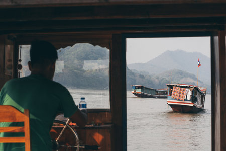 Luang Prabang, Laos - May 2019: view over traditional Laotian wooden slow boats on Mekong river through the window of captain cockpit.のeditorial素材