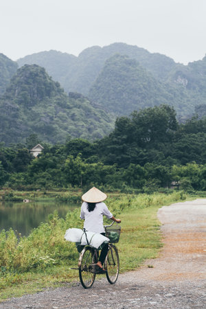 Ninh Binh, Vietnam - May 2019: Vietnamese woman in a rice conical hat riding bicycle in Tam Coc national parkのeditorial素材