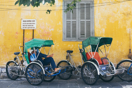 Hoi An, Vietnam - June 2019: Vietnamese rickshaw sleeping in his bicycle cart on the streetのeditorial素材