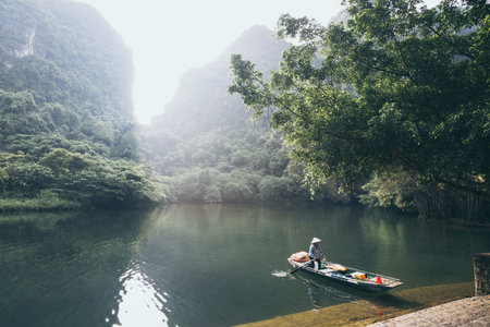Ninh Binh, Vietnam - May 2019: Vietnamese woman in a wooden rowing boat going through Trang An nature park.のeditorial素材