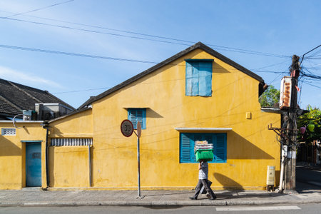 Hoi An, Vietnam - June 2019: street vendor walking by colorful house in old town.のeditorial素材