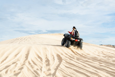Mui Ne, Vietnam - June 2019: off-road ATV quad bike driving through desert sand dunes at sunrise.のeditorial素材