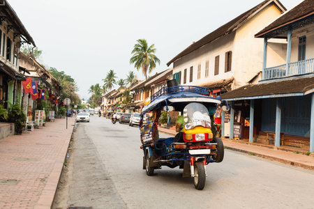 Luang Prabang, Laos - May 2019: tuk-tuk motorcycle taxi riding on the city main street early in the morningのeditorial素材