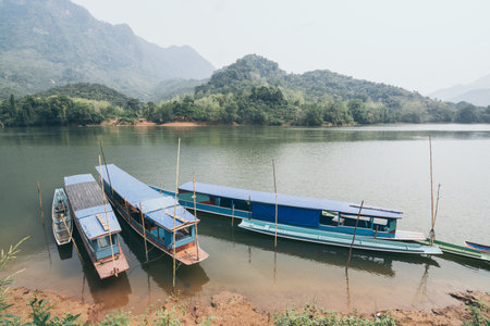 Traditional Laotian wooden slow boat on Nam Ou river near Nong Khiaw village, Laos. Reflection in...