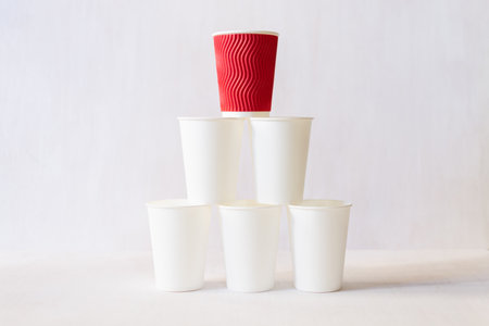Red paper coffee cup stands on top of white paper cups pyramid. White background, copy spaceの写真素材