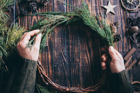 Male hands making Christmas wreath with fir tree brunches on dark wood backgroundの写真素材