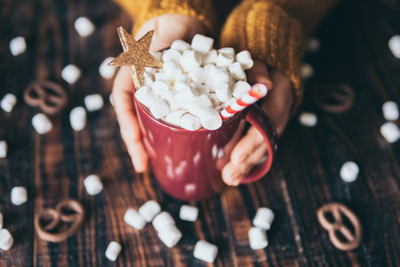 Woman in yellow sweater holding hot chocolate mug covered with marshmallow on dark wood background.の写真素材