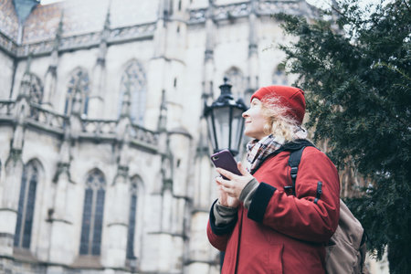 Woman in red coat looking at her mobile phone screen on the street of old European townの写真素材
