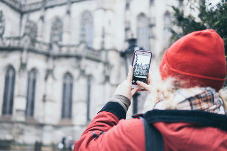 Woman in red coat taking photo of gothic cathedral with her mobile phone on the street of European town Kosice, Slovakiaの写真素材