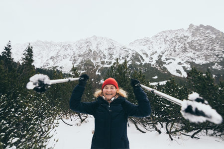 Woman trekking in snowy High Tatra mountains in winter close to Popradske Pleso, Slovakia. Holding trekking poles in her hands and smiling.の写真素材