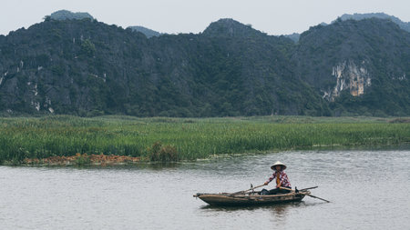 Ninh Binh, Vietnam - May 2019: Vietnamese woman in a wooden rowing boat going through Trang An nature park.のeditorial素材