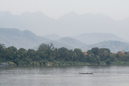 Traditional Laotian wooden slow boats on Mekong river near Luang Prabang at sunset, Laos. Mountain on backgroundの写真素材