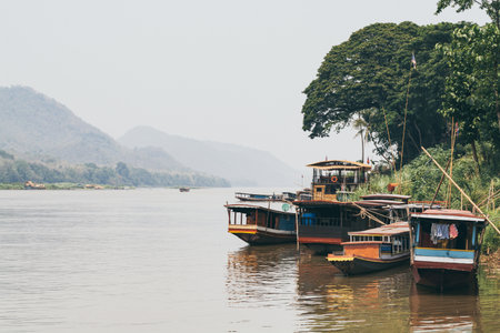 Traditional Laotian wooden slow boats on Mekong river near Luang Prabang at sunset, Laos. Mountain...