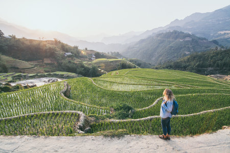 Young Caucasian blonde woman in denim shirt overlooking Sapa rice terraces at sunset in Lao Cai province, Vietnam.の写真素材