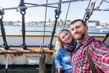 Couple taking selfie with Stockholm waterfront houses through ratlines of sailing ship on background, Swedenの写真素材