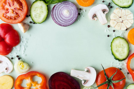 Flat lay pattern of different sliced vegetables on green background. Framed with copy space in the middleの写真素材