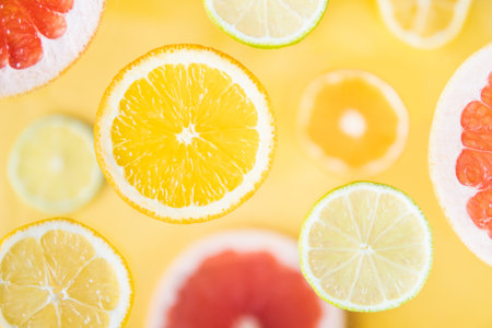 Pattern of different citrus fruit levitating above yellow background. Slices of orange, lemon, lime and grapefruitの写真素材