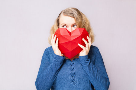 Young woman peeking out of polygonal diamond shaped red heartの写真素材