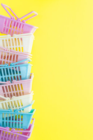 Pile of colourful plastic shopping baskets on a yellow background. Vertical orientationの写真素材