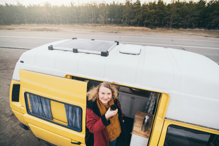 Young blond woman travelling by camper van with solar panel on the roof top and pine forest on the backgroundの写真素材