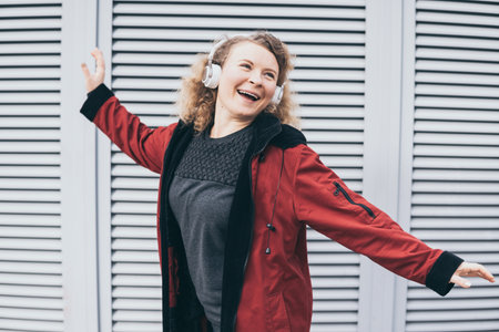 Young blonde woman jumping while listening to music in wireless headphones in the urban environmentの写真素材