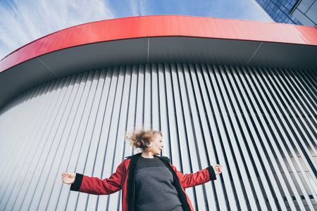 Young blonde woman listening to music in wireless headphones in the urban environment, modern architecture on backgroundの写真素材