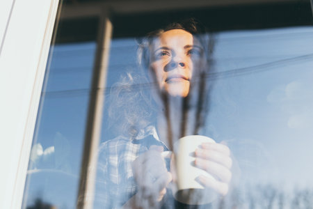 Young blonde woman looking out of the window with a concerned expression on her face. Reflection in the glass, double exposure effectの写真素材