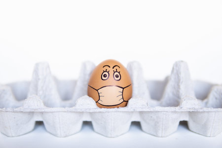 Chicken egg looking out of a tray with doodle face wearing medical mask. Conceptual image of stay at...