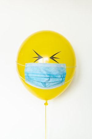 Yellow balloon with a medical mask and doodle closed eyes. Conceptual image of Birthday party during Corona virus quarantine lockdownの写真素材