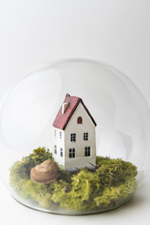 Conceptual image of safety when staying at home during Corona virus COVID-19 quarantine lockdown. Small toy house under the glass with moss and grass around.の写真素材