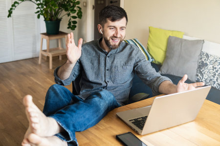 Handsome Eastern European man working from home during Corona virus quarantine lockdown, having online video chat with his colleaguesの写真素材