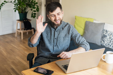 Handsome Eastern European man working from home during Corona virus quarantine lockdown, having online video chat with his colleaguesの写真素材