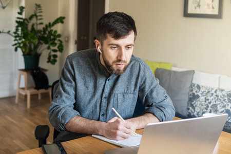 Handsome Eastern European man studying remotely at home during Corona virus quarantine lockdown, writing down during online coursesの写真素材