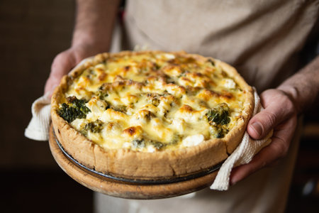 Male hands holding cheese and broccoli quiche tart. Home cooking according to French recipe.の写真素材