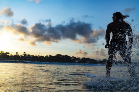 Silhouette young adult surfer rides the waves of ocean at the sundownの写真素材