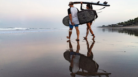 Two surfers man and beautiful girl with surfboards look at sunriseの写真素材