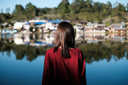 asia women traveller stand near reflect lake looking out to view of old house and sun ray shining her hair  at ban ruk thai Mae Hong Son Thailandの写真素材
