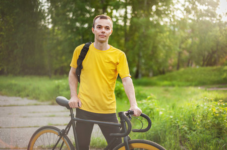 A young Man stopped to rest With his Bicycle in a public Park. He enjoys an early Sunny morning in the forest.の写真素材