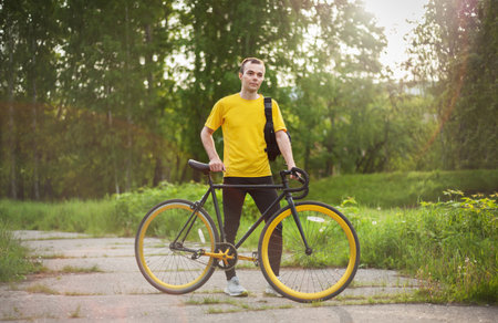 A young Man stopped to rest With his Bicycle in a public Park. He enjoys an early Sunny morning in the forest.の写真素材